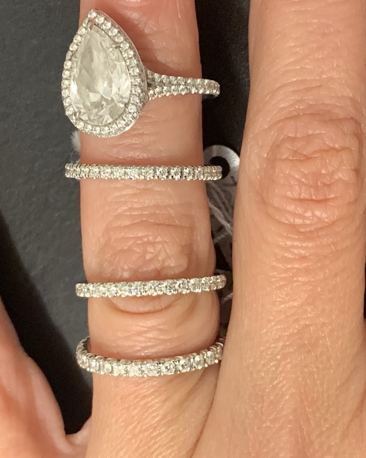 Three pavé eternity bands worn on separate fingers beneath a pear halo engagement ring