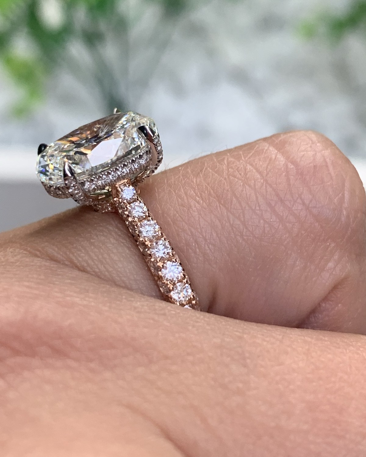 Profile view of a cushion-outline diamond above a hidden halo on a warm rose gold pavé shank