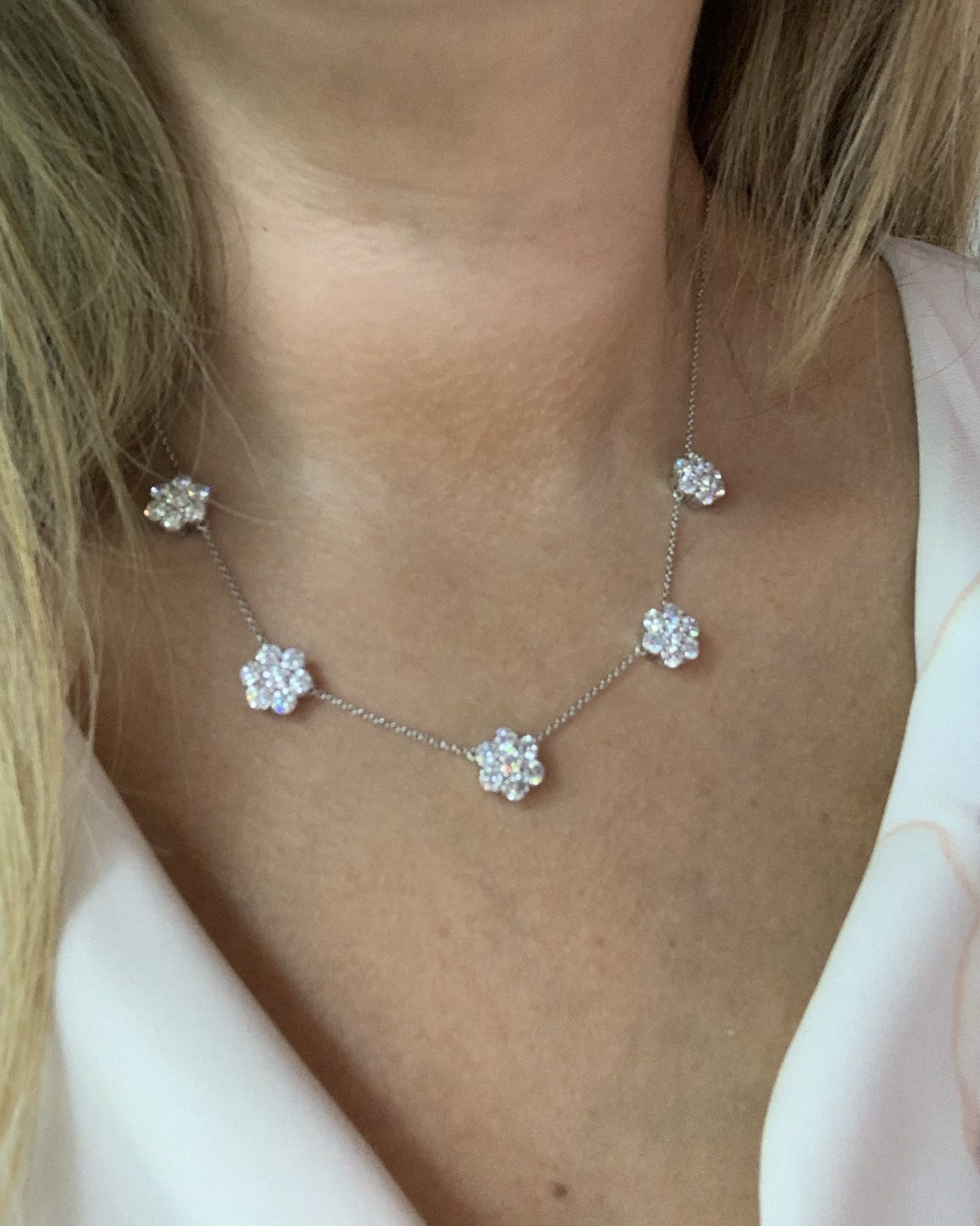 Station necklace hung with round diamond flower clusters on a fine chain, worn at the collarbone
