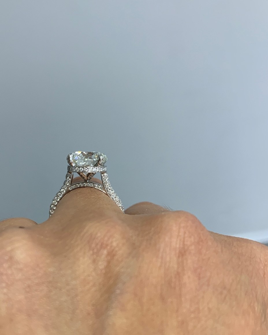 Profile view of an oval diamond solitaire showing the hidden halo beneath the center stone and the pavé shank