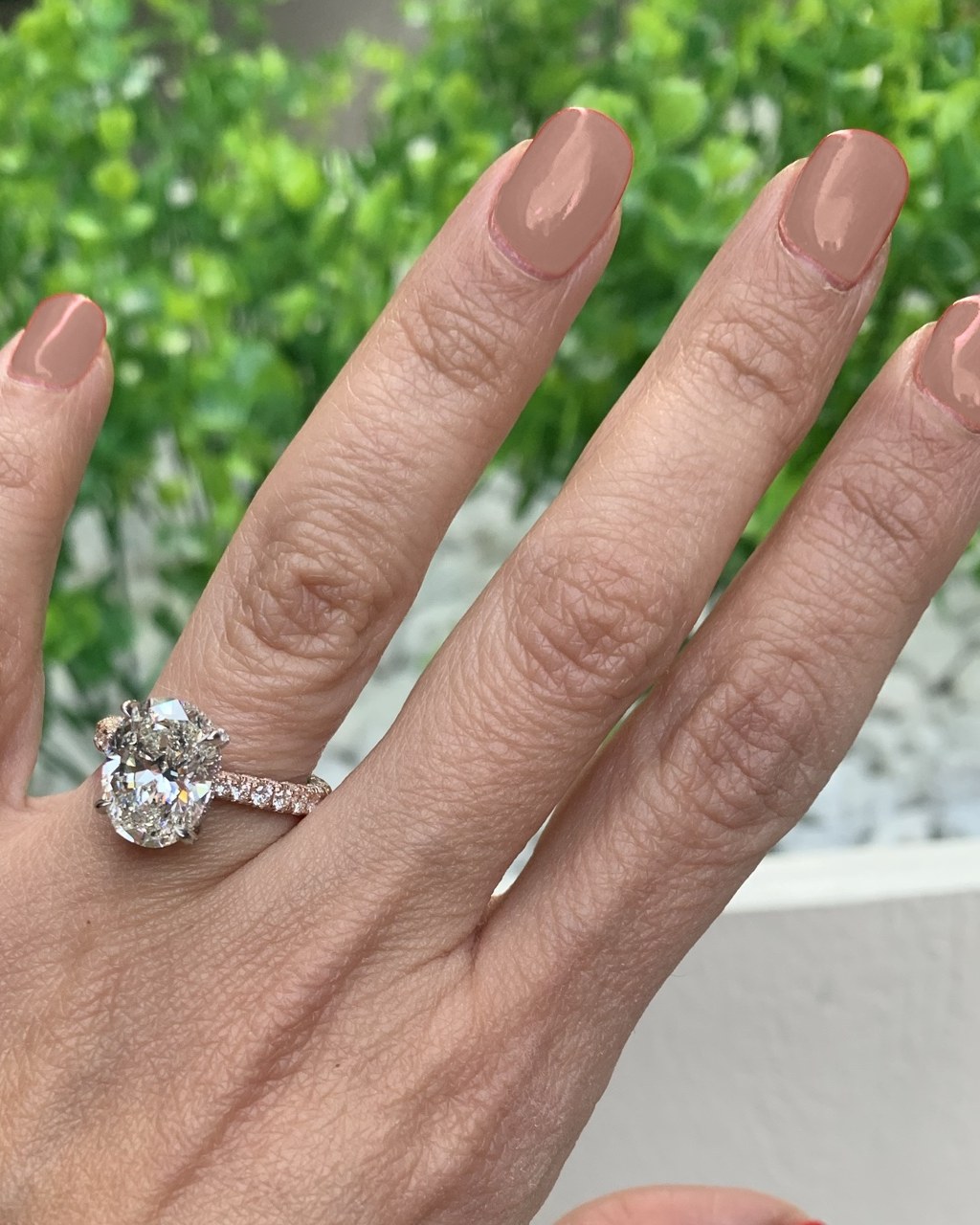 Angled view of the oval hidden-halo ring on its rose gold shank, worn on the hand