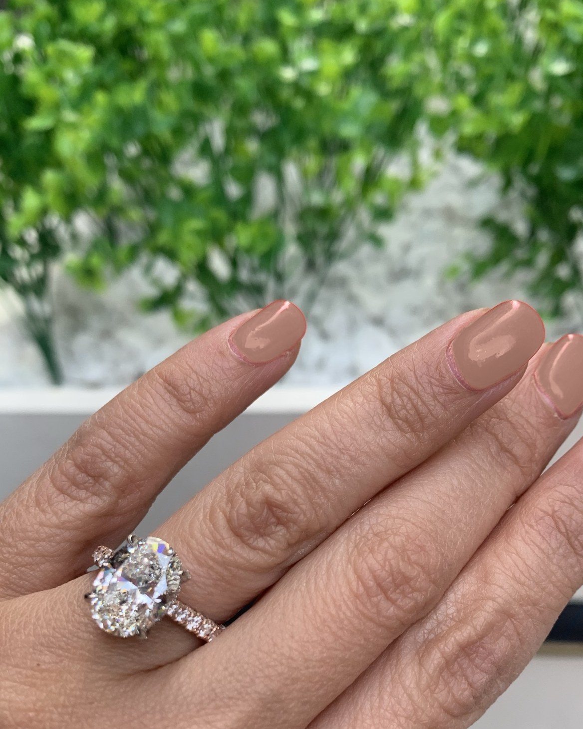 Oval diamond with a hidden halo on a warm rose gold pavé shank, worn on the hand outdoors