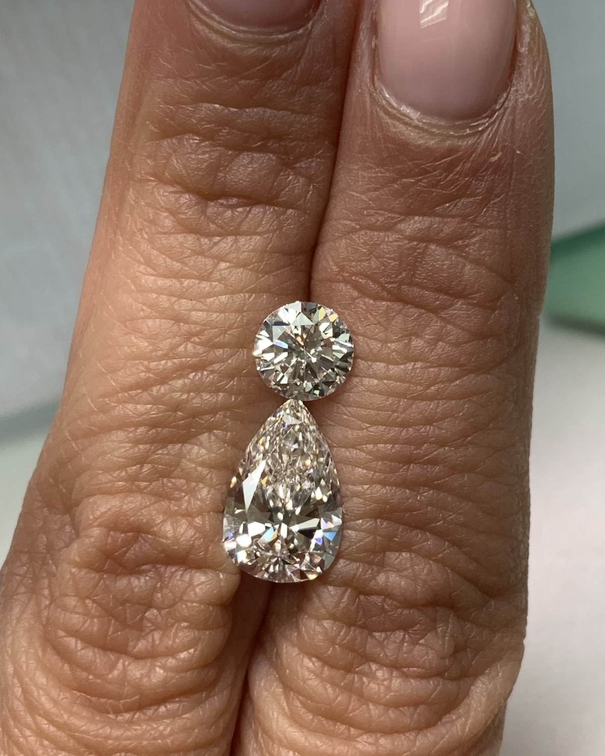 Drop earring with a round brilliant above an articulated pear-shape diamond, held between the fingers