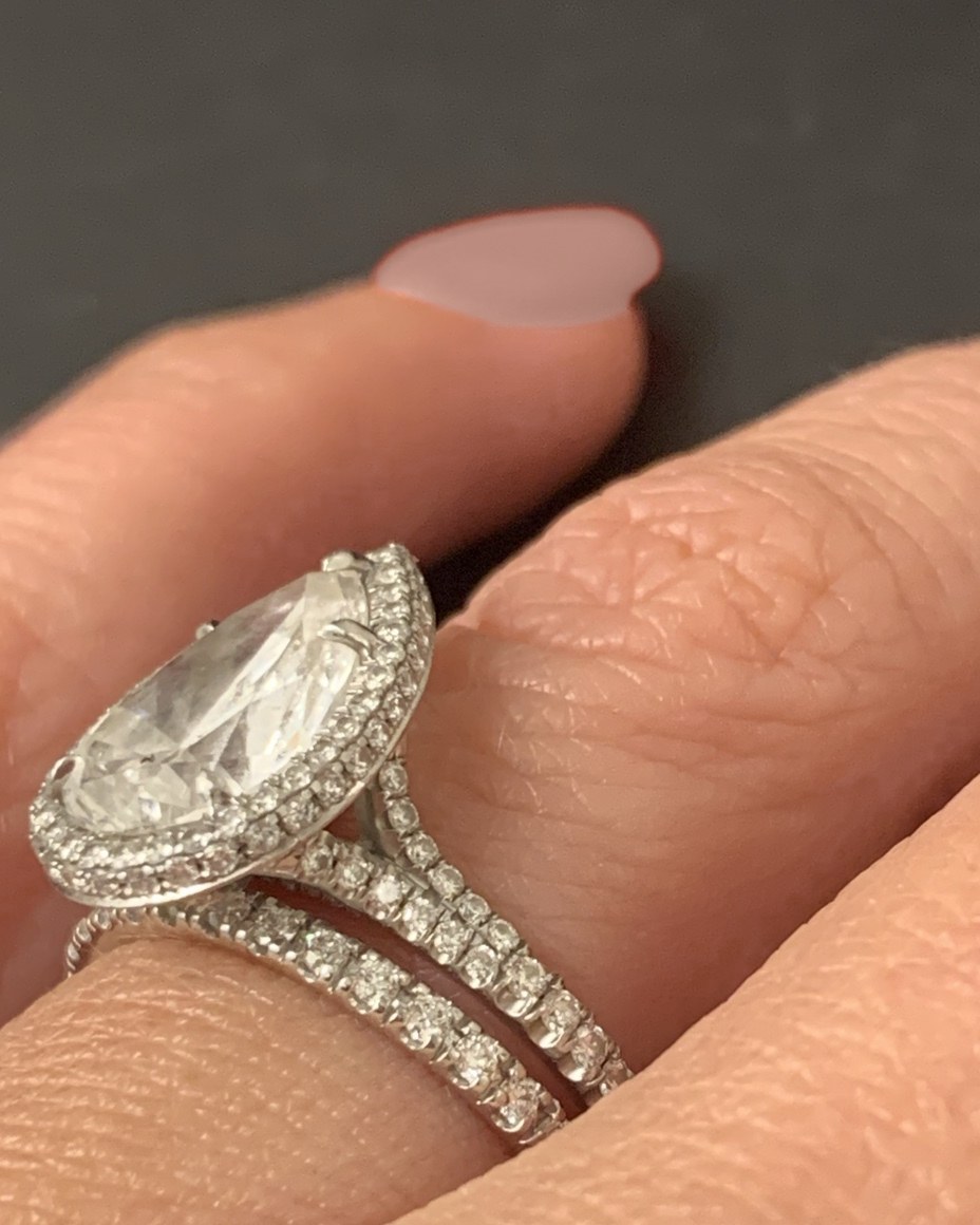 Angled view of the pear halo engagement ring and its matched pavé band on the hand