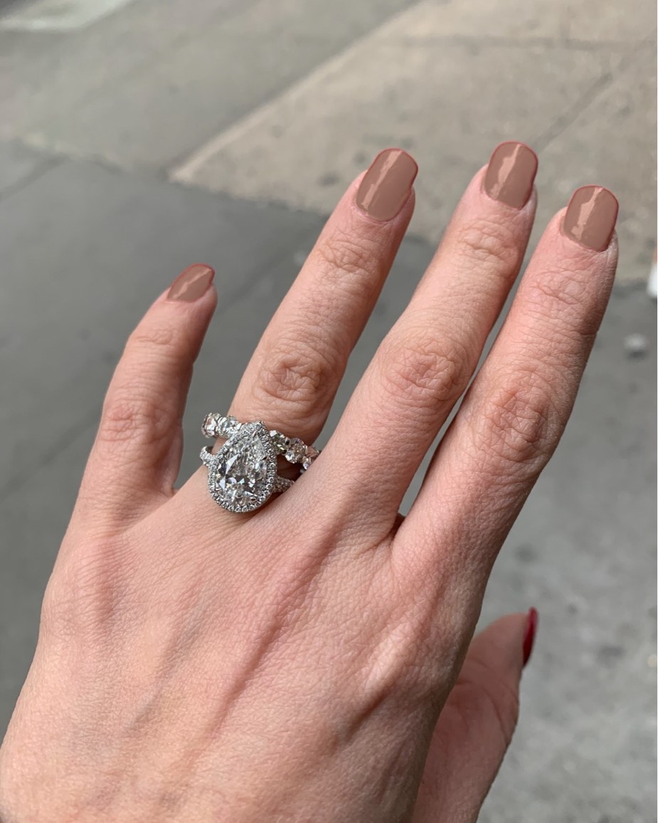 The pear halo ring and matched band worn on the hand outdoors on a city sidewalk