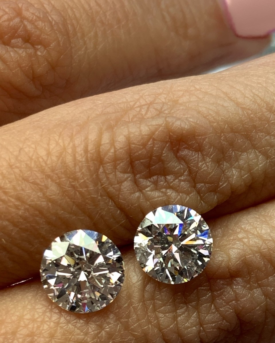 A matched pair of round brilliant diamond studs held between the fingers, face up