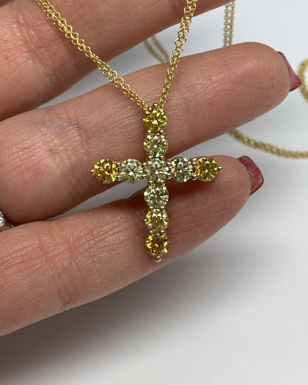 Cross pendant set with yellow round diamonds on a fine yellow gold chain, held in the fingers