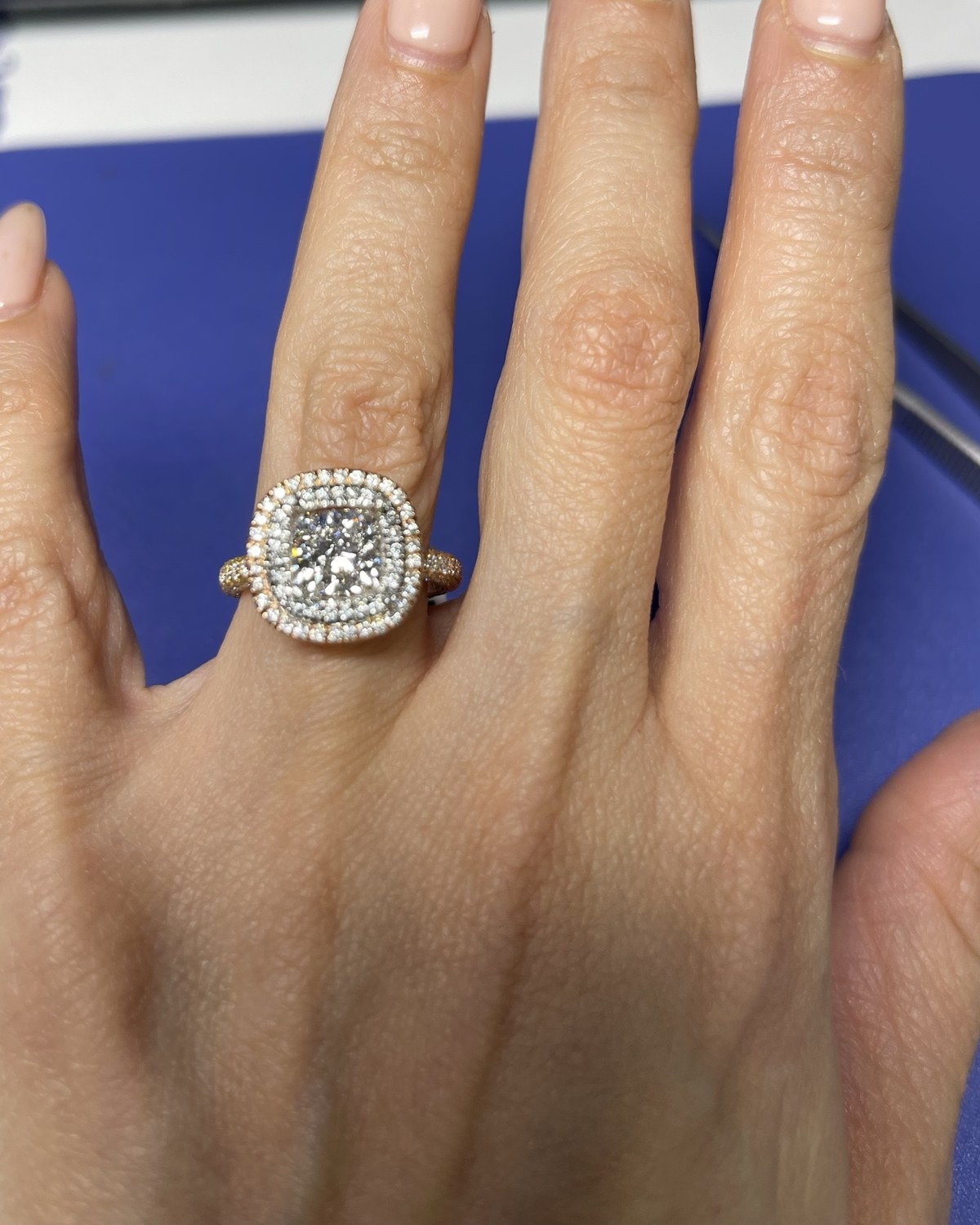 Cushion-cut diamond in two colorless halos on a rose gold basket and fine pavé shank, worn on the hand