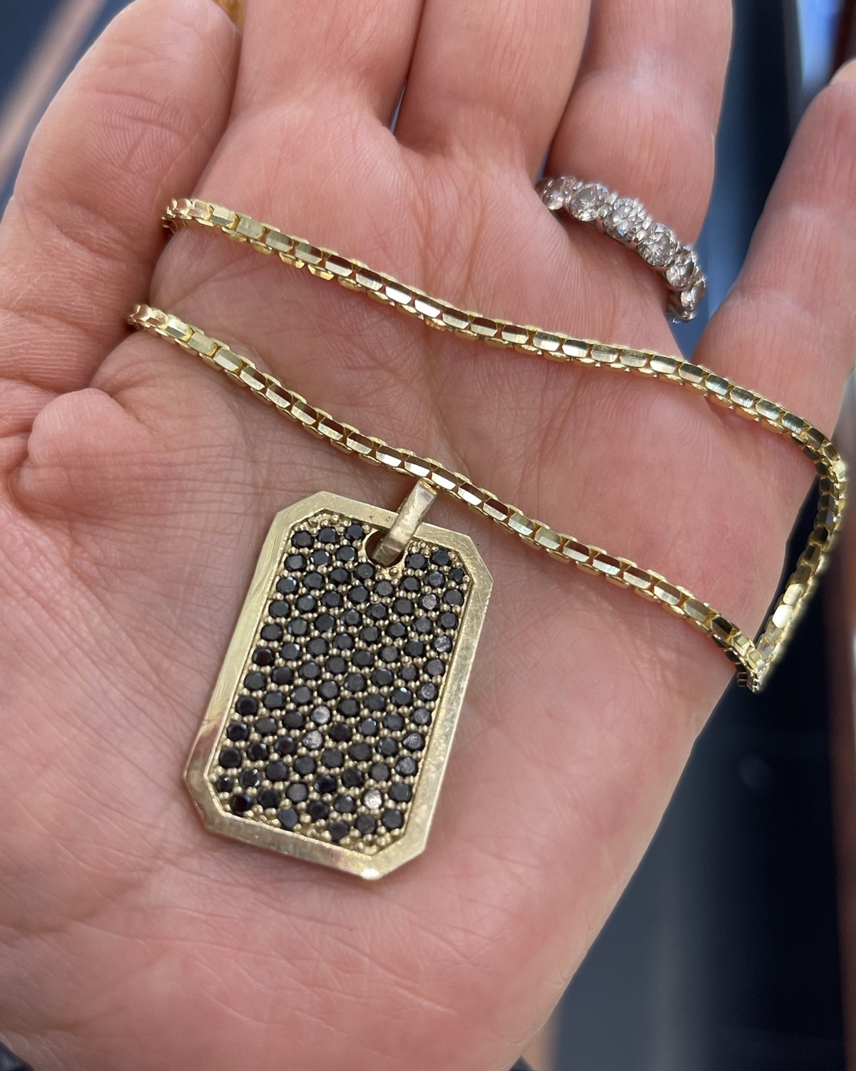 Yellow gold cut-corner dog tag pendant paved across its face with small dark stones, on a heavy yellow chain