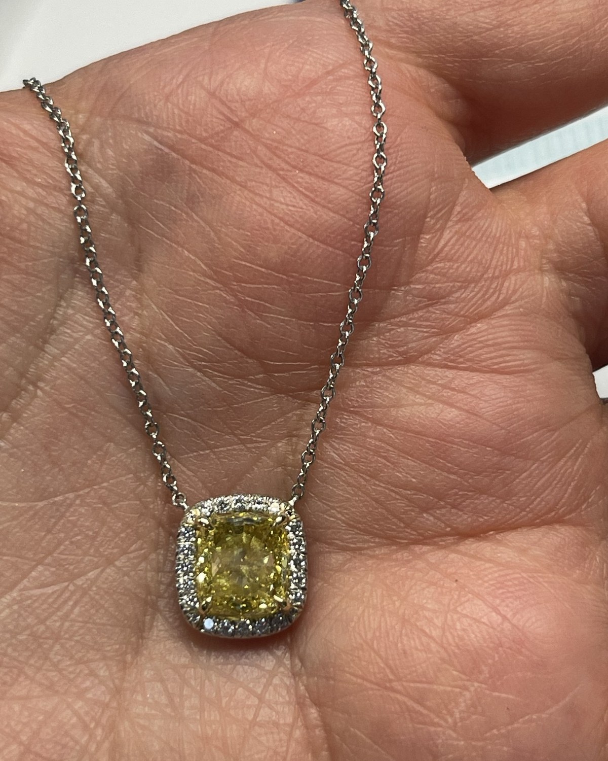 Yellow cushion-cut diamond in a colorless pavé halo on a fine white chain, held in the palm