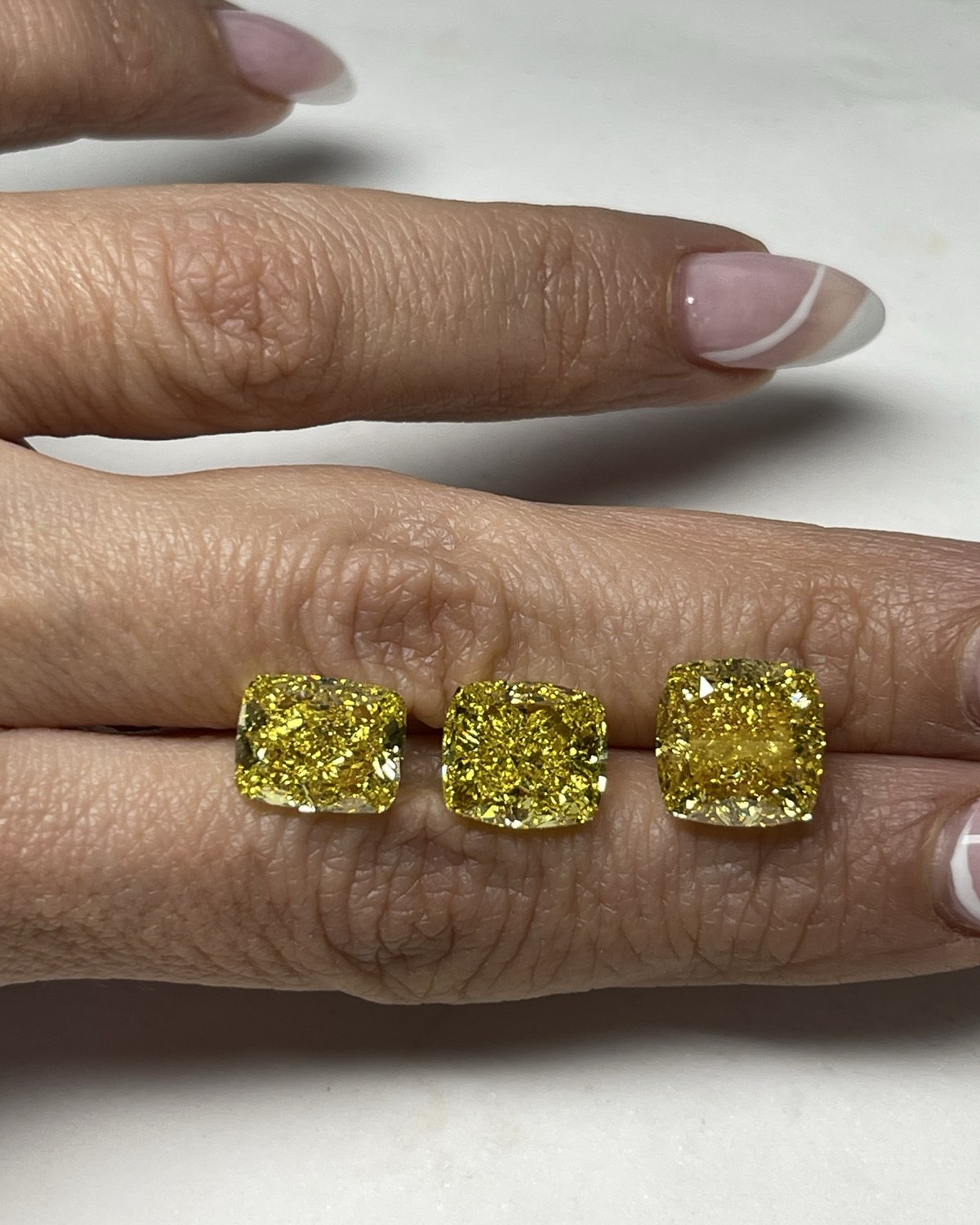 Three loose yellow cushion-cut diamonds of graduated size held between the fingertips