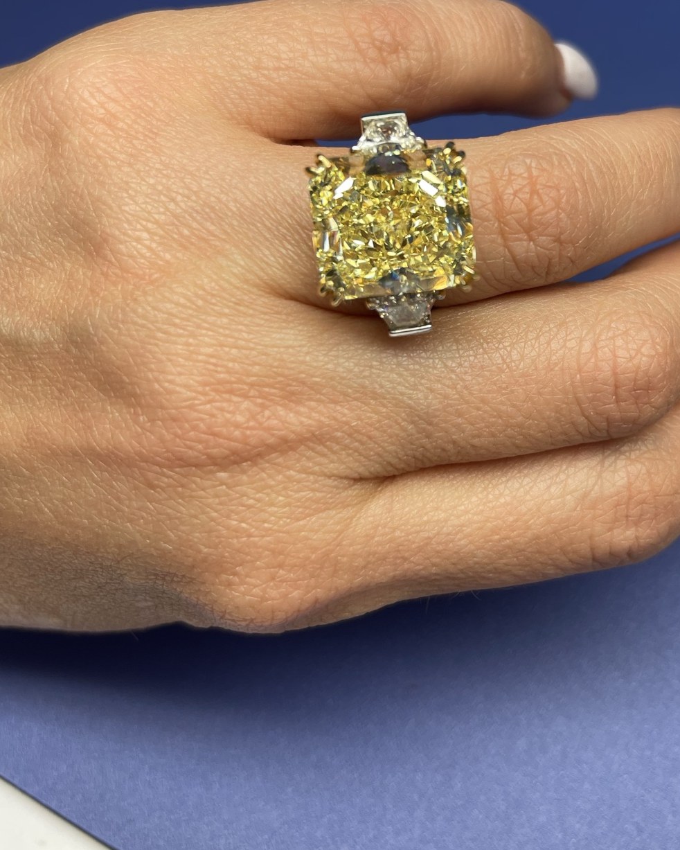 Large yellow cushion-cut diamond between two colorless step-cut shoulder stones in a yellow gold basket, worn on the hand