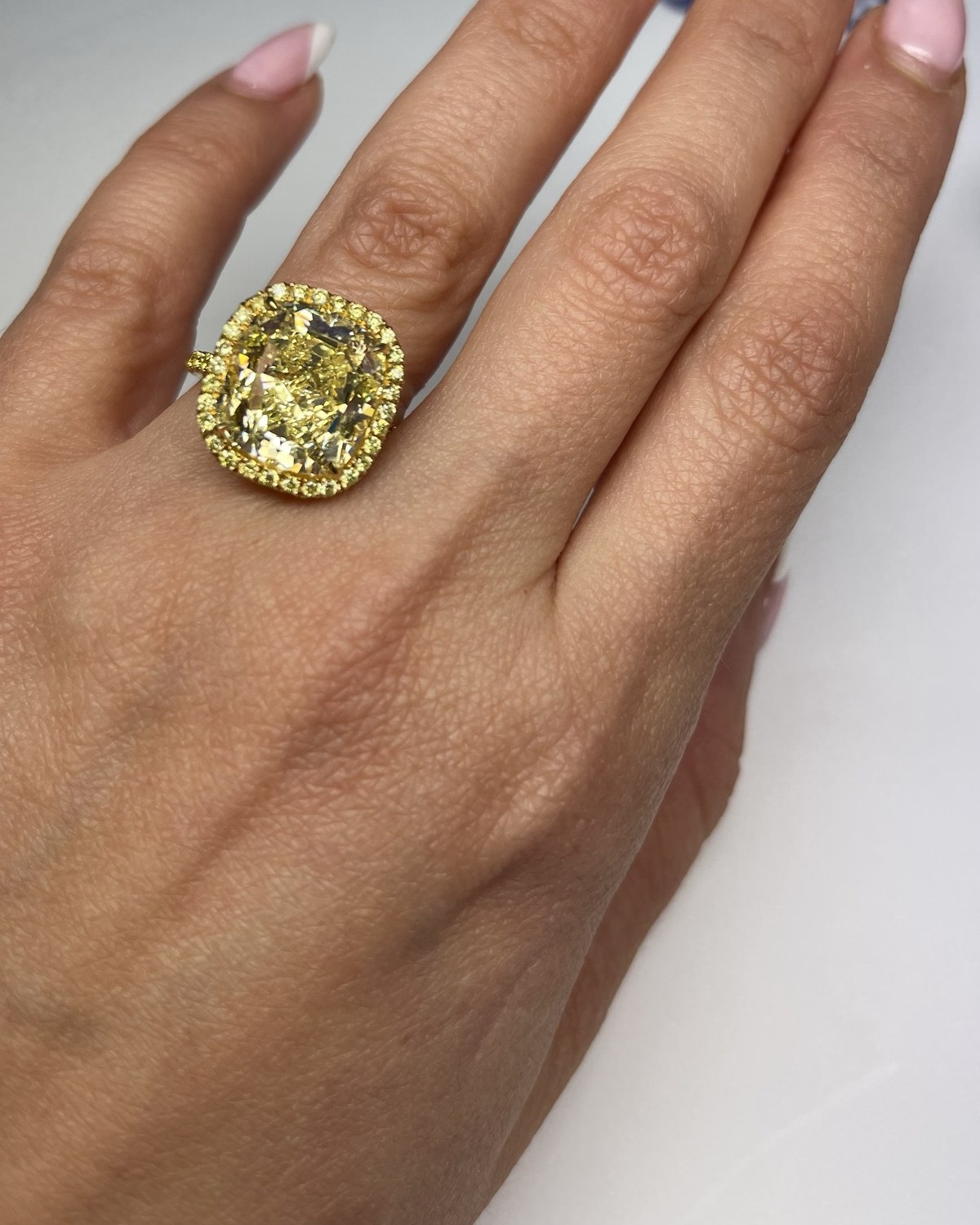 Yellow cushion-cut diamond inside a halo of yellow gold and small yellow stones, worn on the hand