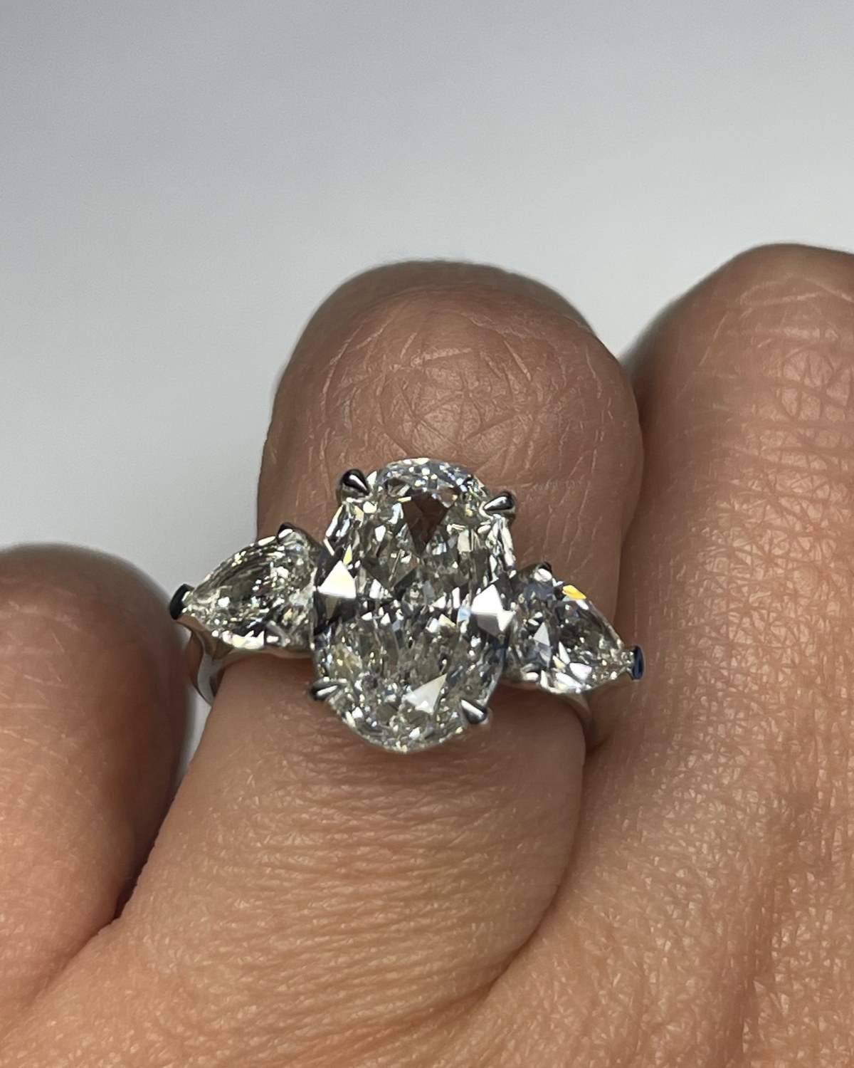 Close view of an oval brilliant diamond between two pear-shape side stones on a plain white shank