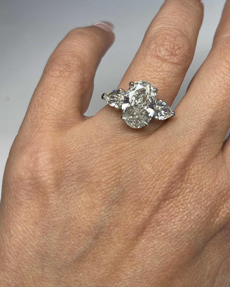 Oval three-stone ring with pear shoulders worn on a flat open hand