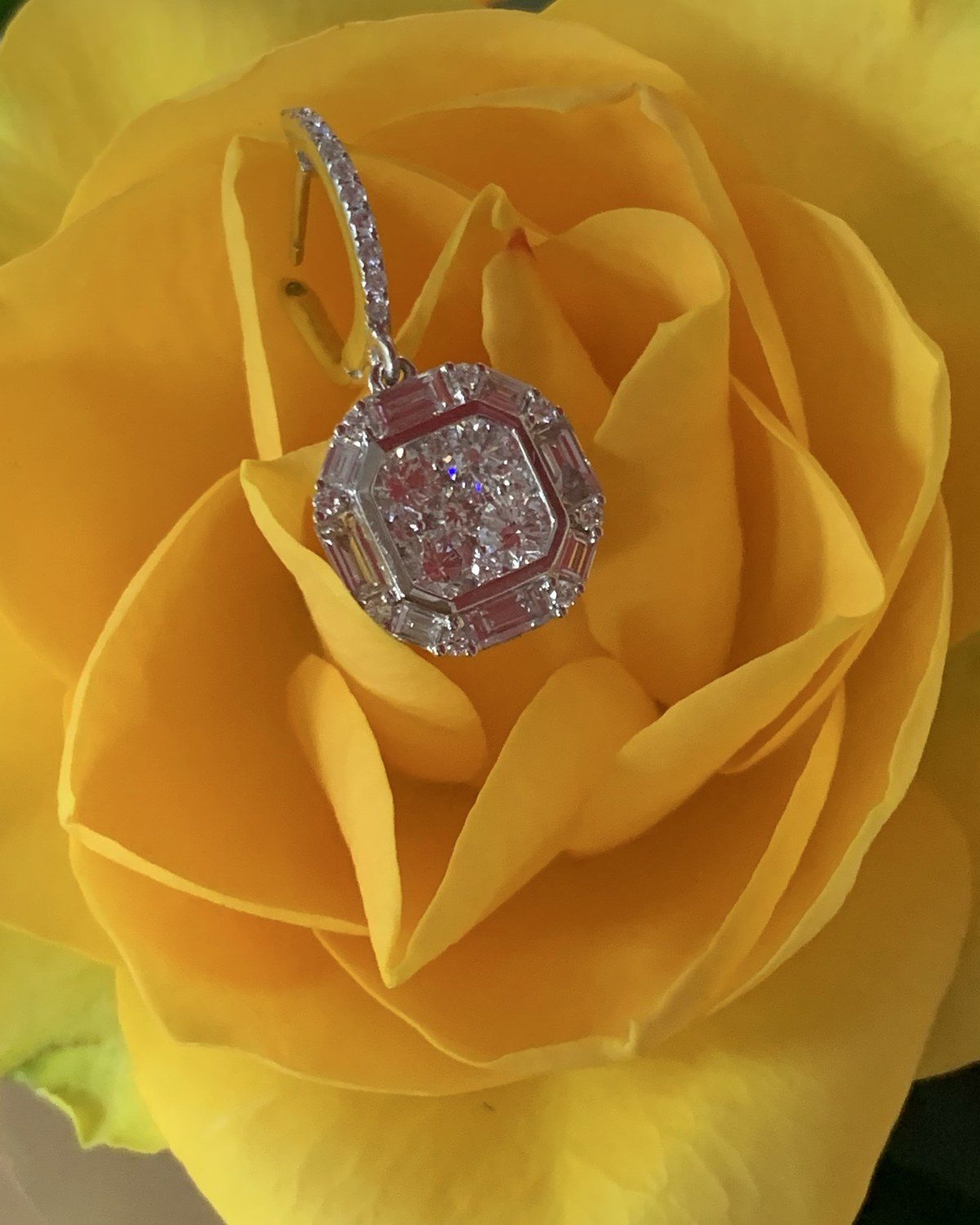Cushion-outline diamond cluster pendant on a fine chain, resting in the petals of a yellow rose