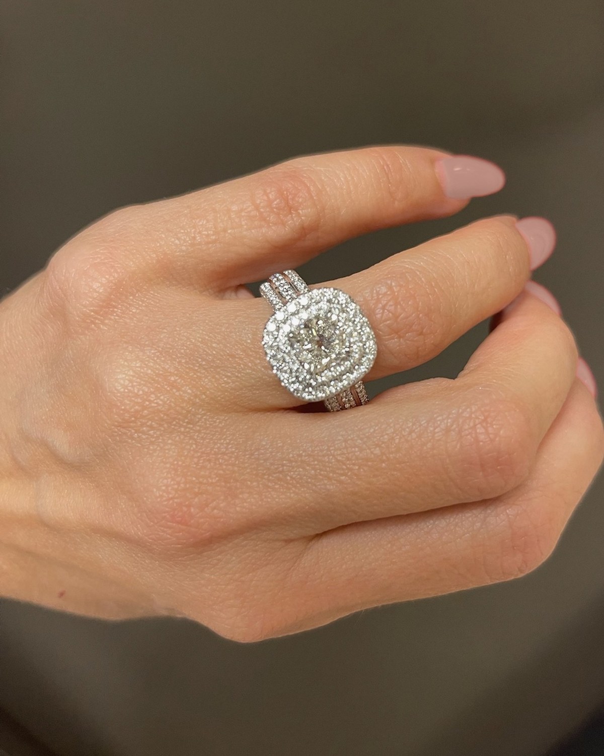 Cushion-cut diamond in a double halo above a three-row pavé shank, worn on the hand