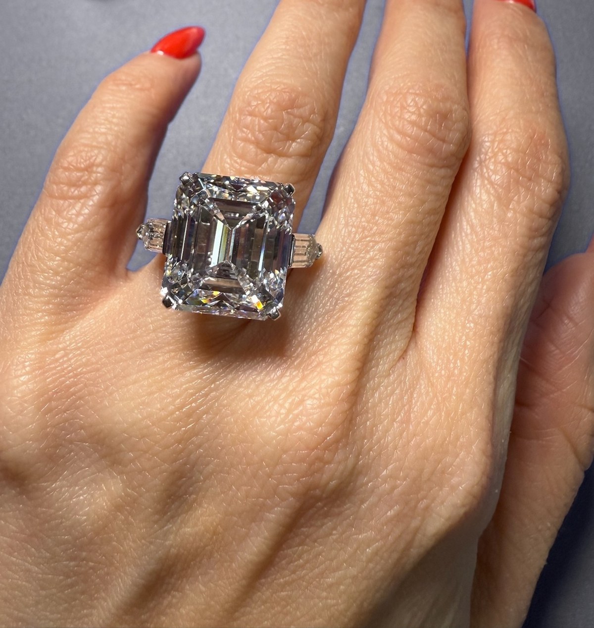 Face-up view of a large step-cut diamond three-stone ring with tapered baguettes, worn on the hand