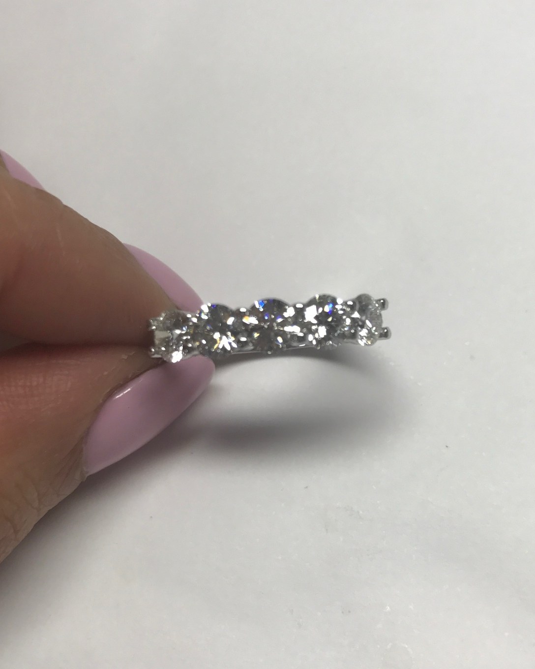 Oval diamond band with the stones set east-west, held between the fingers against white