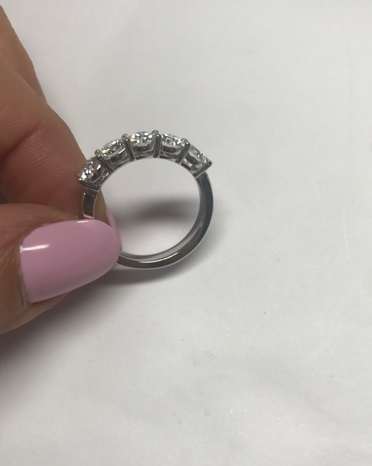 Profile view of the oval diamond band held between the fingers, showing how low the stones sit