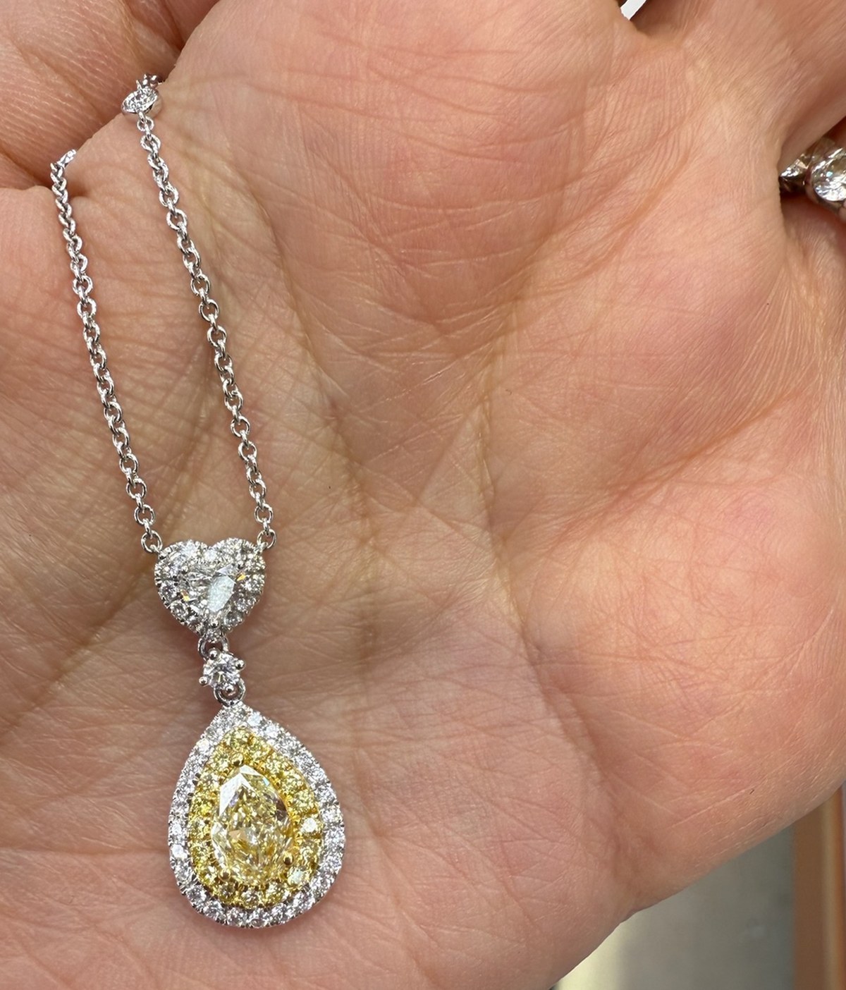 Fancy yellow pear-shape diamond pendant in a double halo of yellow and white diamonds, on a white gold chain, held in the palm