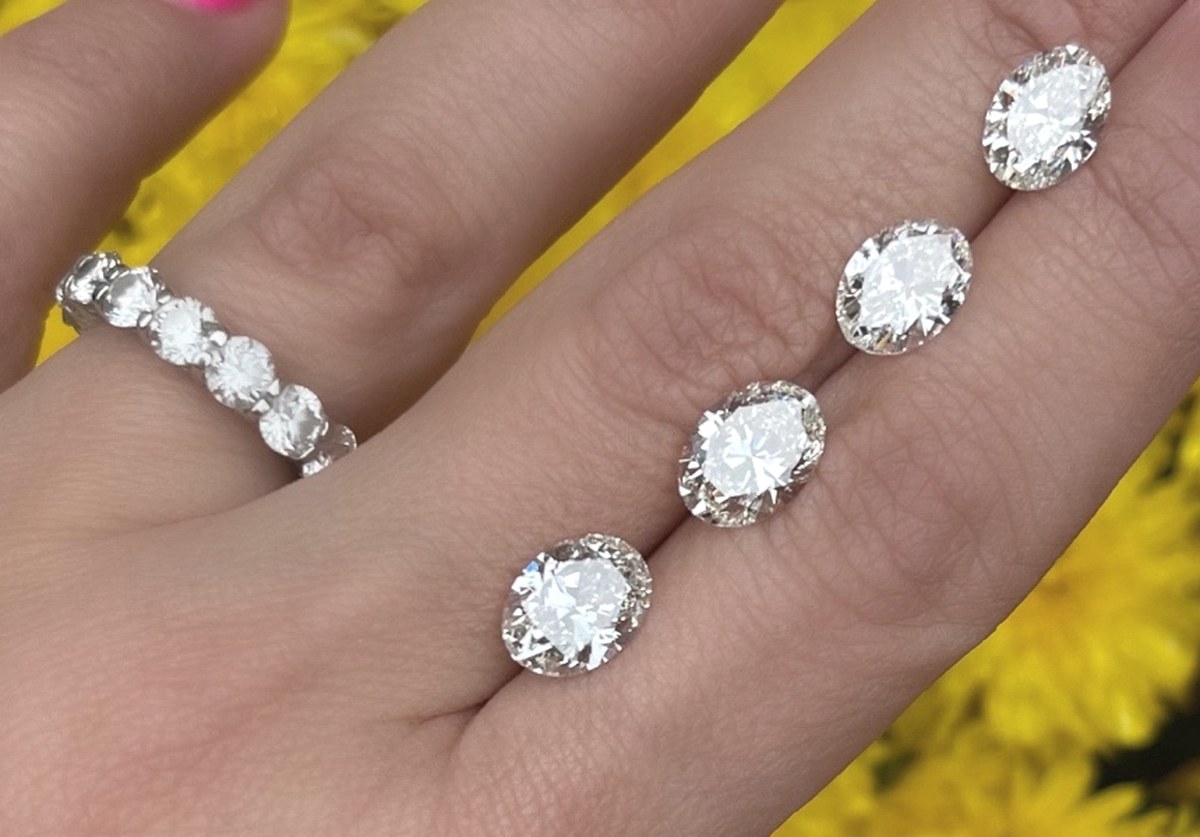 Four loose oval diamonds laid across the fingers beside a diamond eternity band