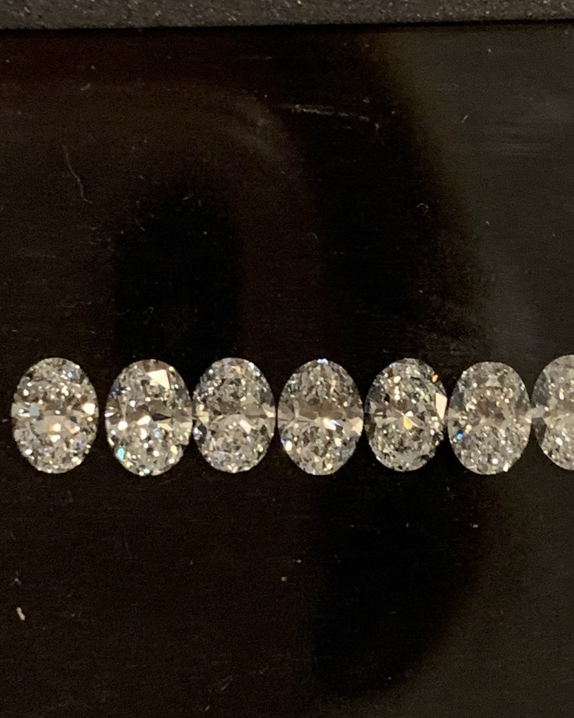 A row of loose oval brilliant diamonds laid side by side on a dark display tray