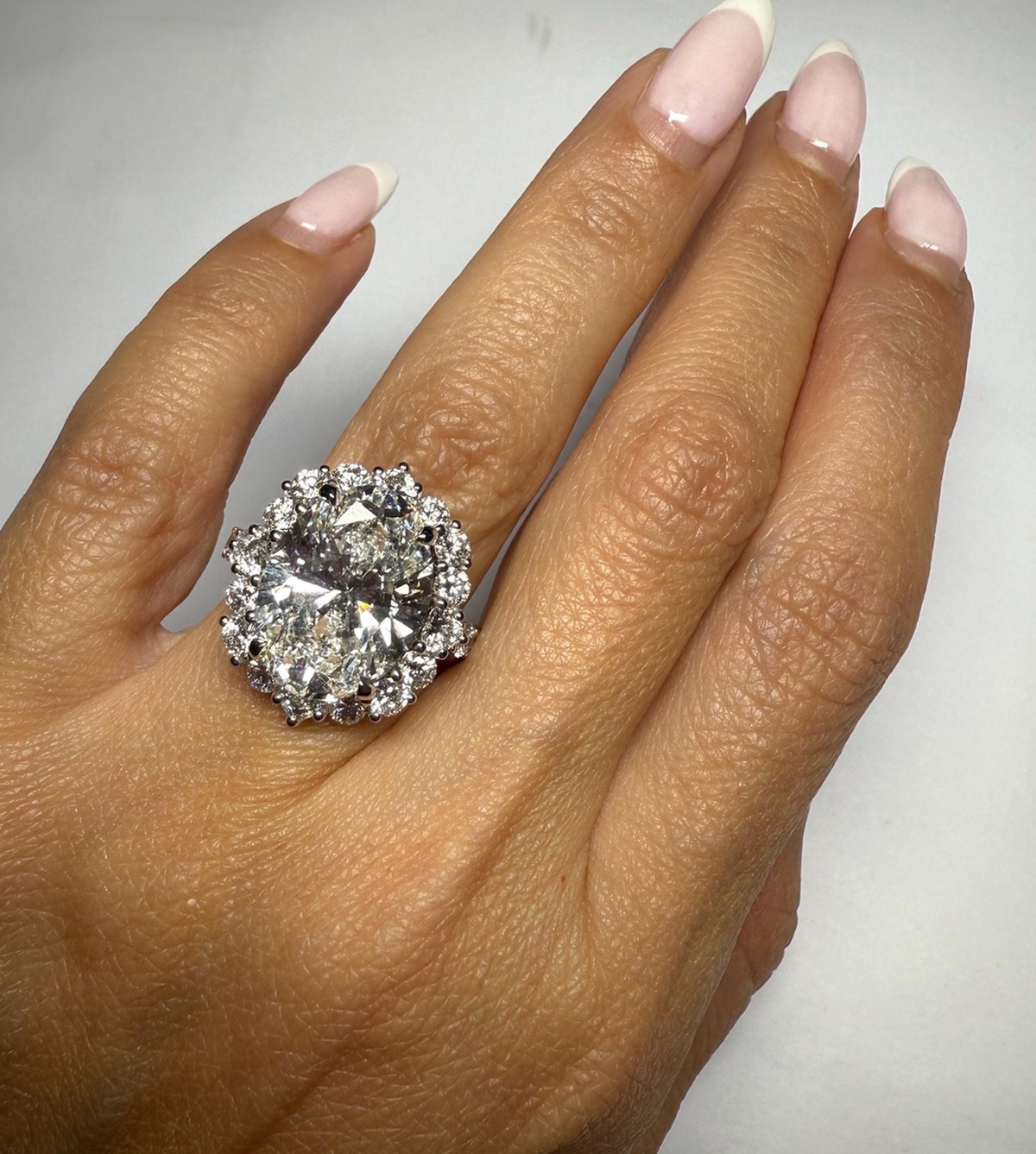 Large oval diamond in a claw-set round diamond halo, worn on the hand in daylight