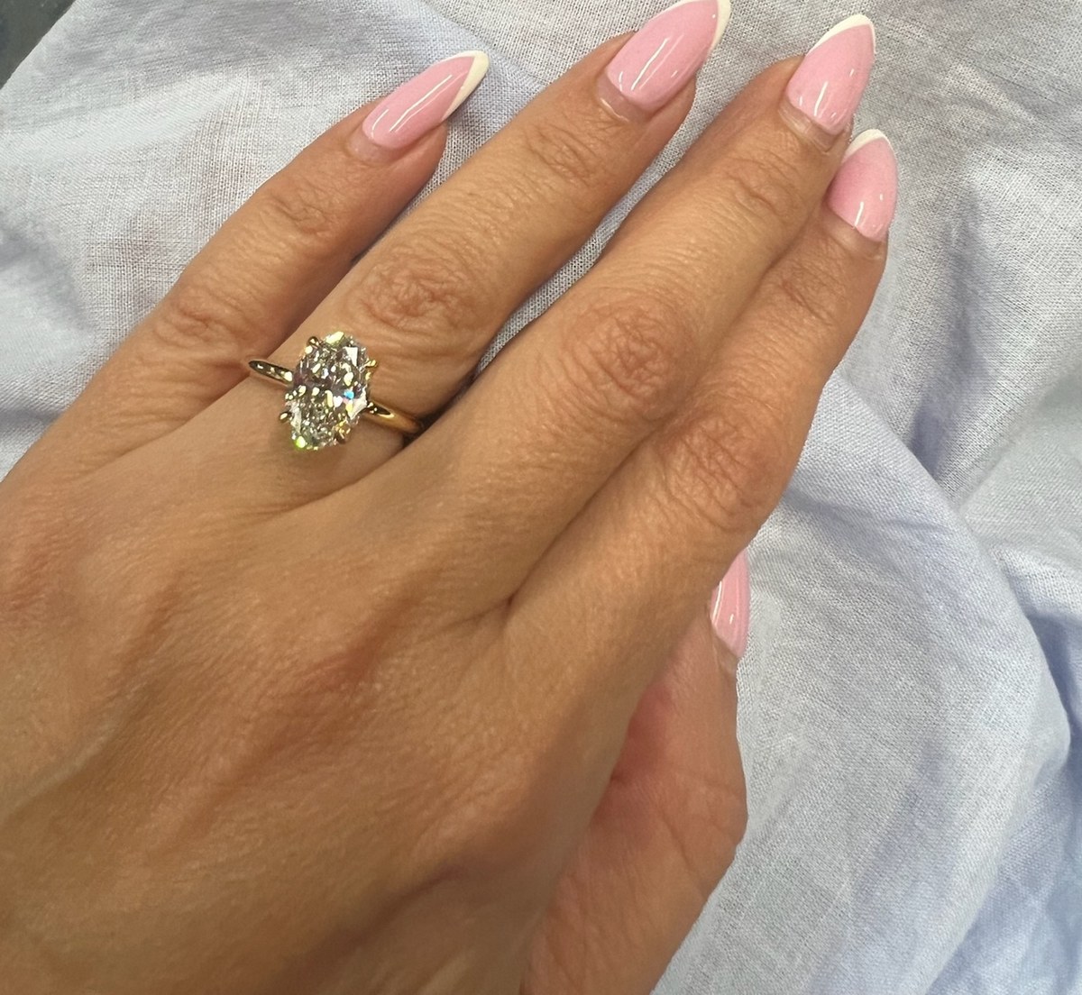 Oval diamond solitaire in yellow gold worn on the hand against white linen