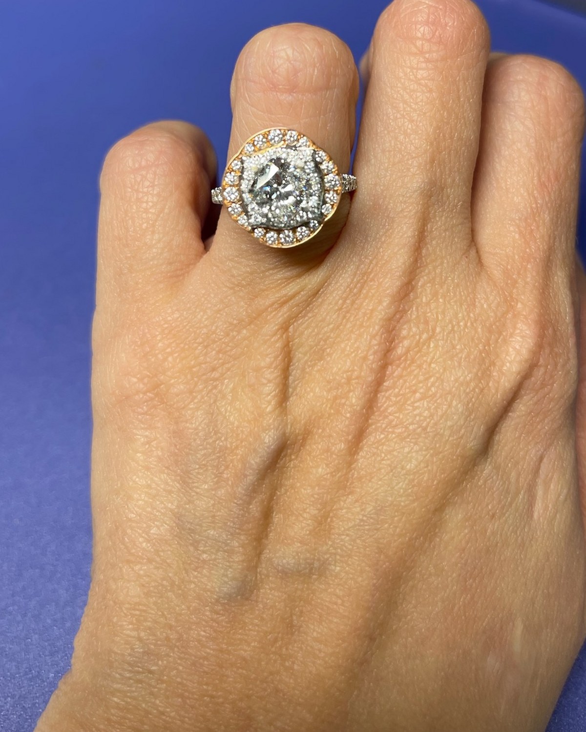 Cushion diamond in a white inner halo ringed by a scalloped rose gold outer halo, worn on the hand