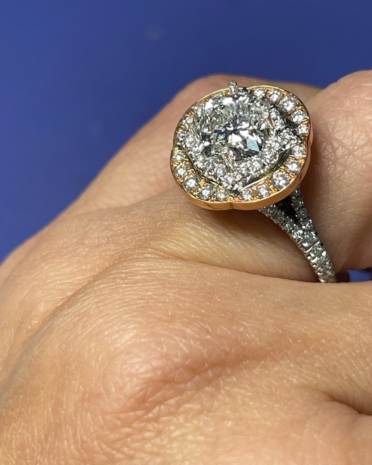 Three-quarter view of a cushion halo ring with a scalloped rose gold outer halo and a pavé shank