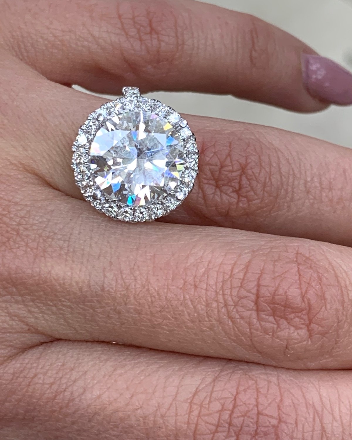 Close view of the large round brilliant halo ring worn on the hand, seen face on