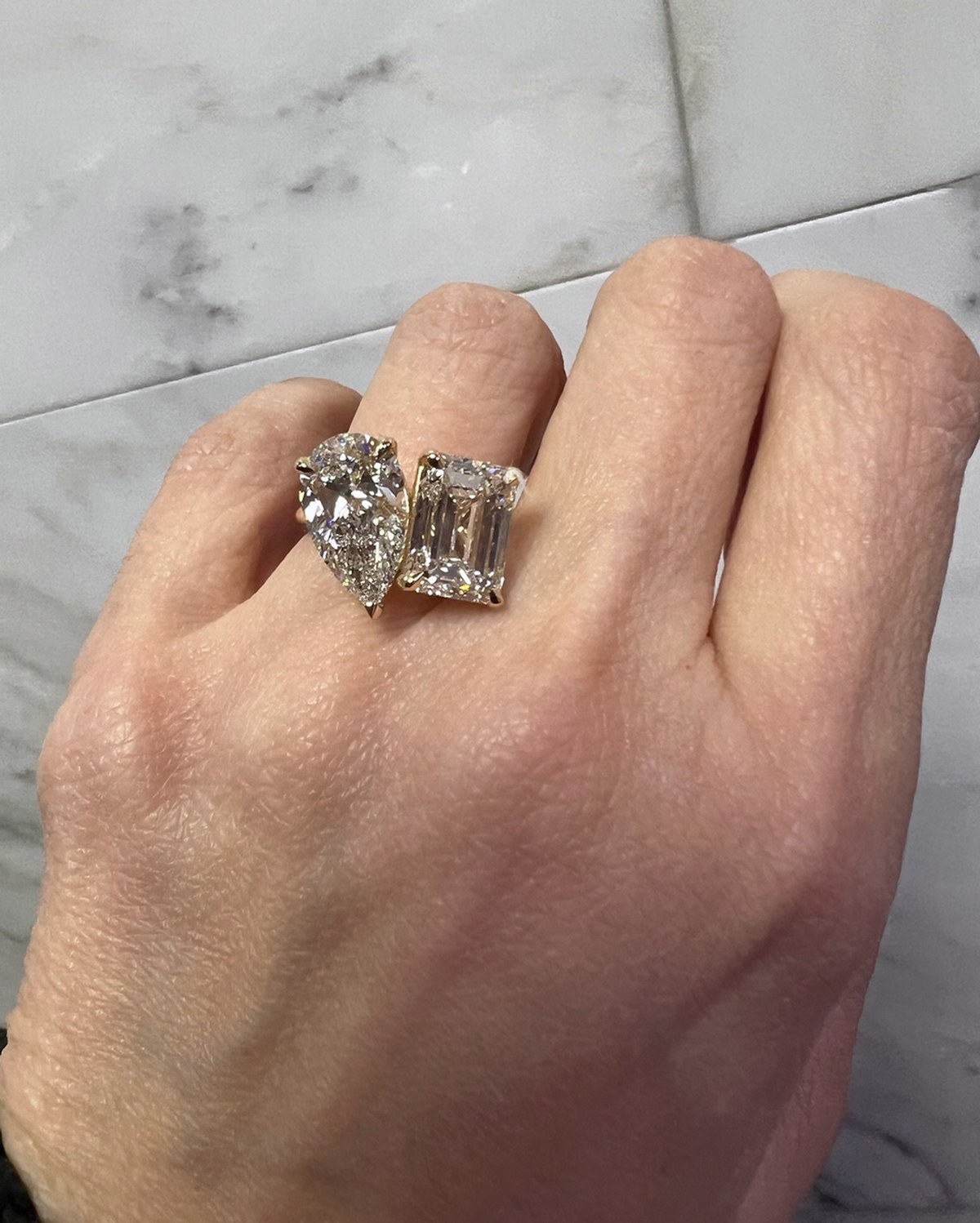 Two-stone ring pairing a pear brilliant with a step-cut diamond on a slim band, worn on the hand
