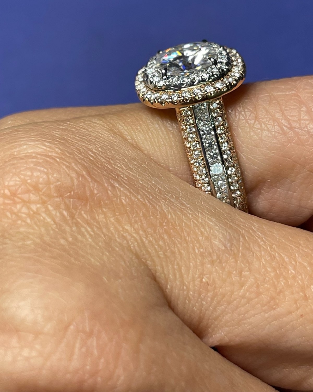 Oval diamond in a double halo with rose gold accents above a wide three-row pavé shank