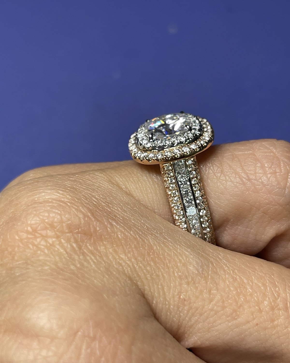 Wider view of the oval double halo ring with rose gold accents and its three-row pavé shank on the hand