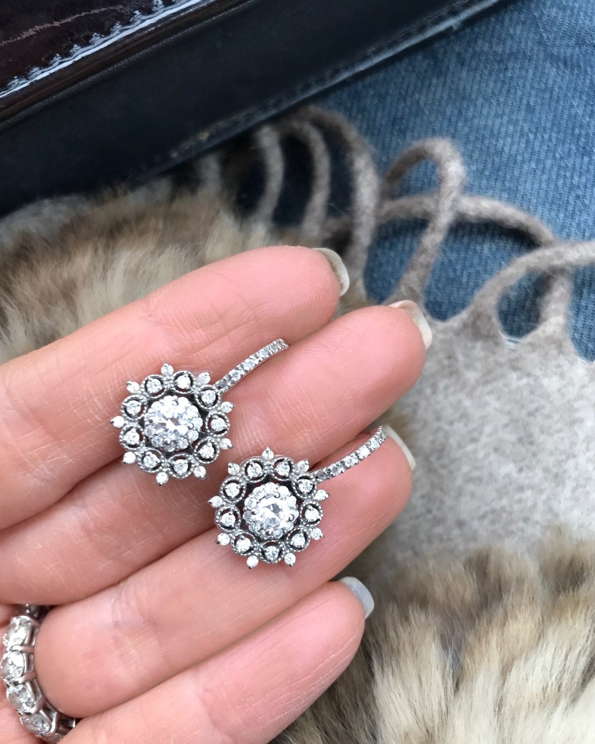 Pair of white gold floral diamond cluster earrings held in the hand against a fur collar